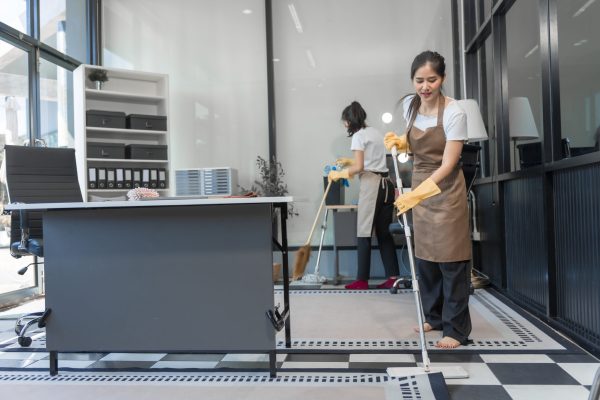 Two Asian housekeepers wear overalls and work together efficiently to clean the living room, study